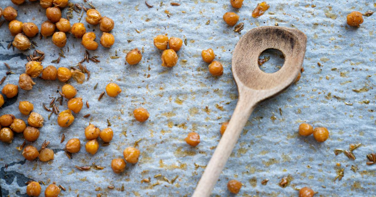fried chickpeas scattered on a baking paper with wooden spoon and hole in the spoon and some caraway or cumin seeds speckled