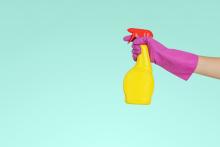 turquoise background yellow spray bottle held by pink rubber glove hand ready to spray