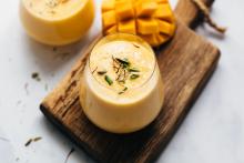 Mango lassi on wooden chopping board with mango on the side yummy looking creamy right thick